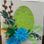 wielkanocna kartka okolicznościowa z zielonym jajkiem ozdobionym zielonymi liśćmi i dwoma niebieskimi kwiatkami