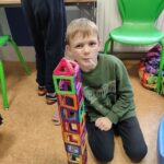 chłopiec siedzi na podłodze przy zbudowanej przez siebie wieży z klocków magnetycznych