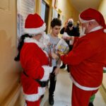 Święty Mikołaj wraz z pomocnikiem wręczają prezent uczniowi.