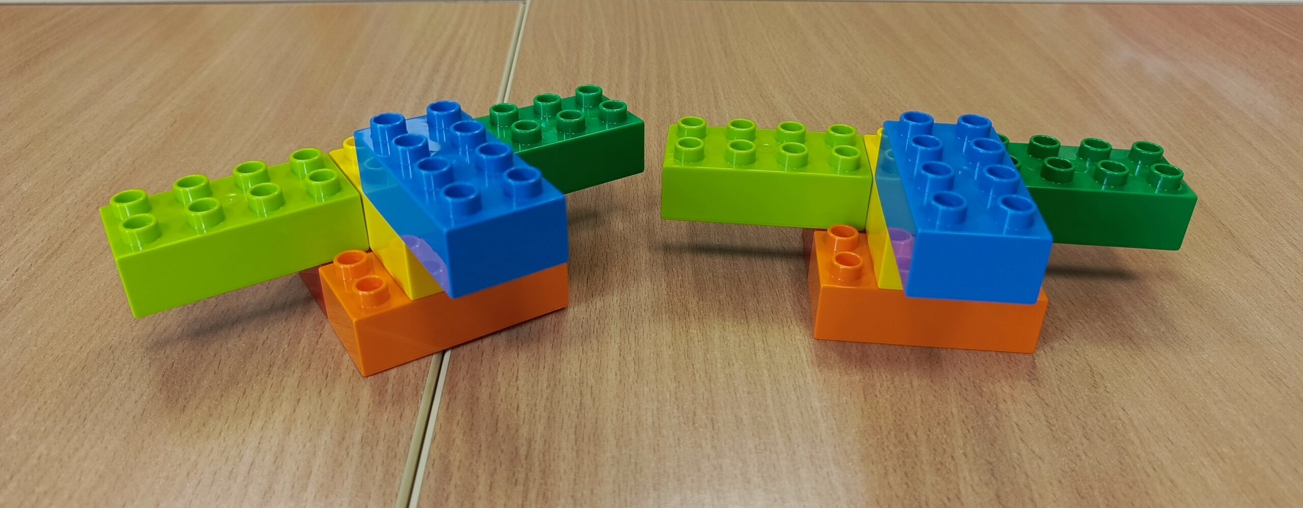 Na zdjęciu widoczne dwa zestawy pięciu klocków w kolorach: niebieski, jasny zielony, ciemny zielony, pomarańczowy, żółty. Złączone klocki kształtem przypominają samolot.