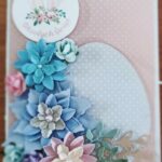 kartka wielkanocna wykonana techniką scrapbookingu z różowym tłem w białe kropeczki i szarym jajkiem ozdobione niebieskimi kwiatkami