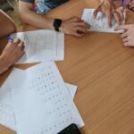 uczniowie siedzą przy stoliku i rozwiązują łamigłówki