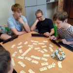 uczniowie siedząc przy stole grają w rummikuba