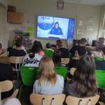 Zdjęcie przedstawia uczniów siedzących w klasie i oglądających połączenie on-line  z astronautą Sławoszem Uznańskim-Wiśniewskim przebywającym w kosmosie.