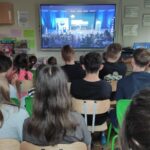 Zdjęcie przedstawia uczniów siedzących w klasie i uczestniczących w połączeniu on-line  z astronautą Sławoszem Uznańskim-Wiśniewskim przebywającym na Międzynarodowe Stacji Kosmicznej