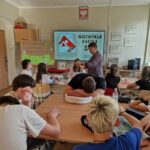 nauczycielka rozdaje uczniom siedzącym w ławkach materiały potrzebne do wykonania kartek