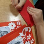 uczennica wypisuje życzenia na kartce laurce dla powstańca