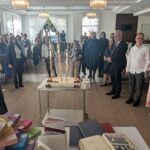 goście stoję w kręgu na środku sali jest wielki tort jubileuszowy