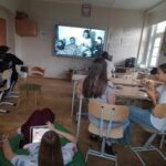 uczniowie siedząc w ławkach w klasie oglądają film