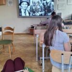 uczniowie siedzący w klasie oglądają na ogromnym monitorze fil dotyczący powstania warszawskiego