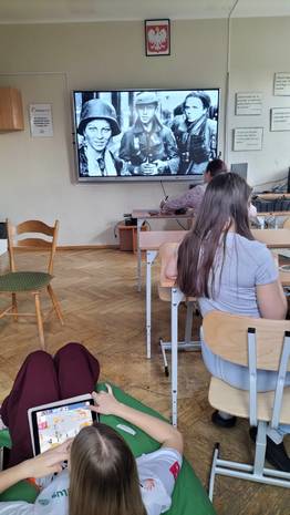 uczniowie siedzący w klasie oglądają na ogromnym monitorze fil dotyczący powstania warszawskiego