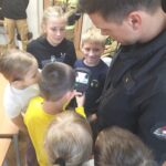 Zdjęcie przedstawia uczniów klasy 1-3 SP wraz ze strażakiem Komendy Miejskiej Straży Pożarnej w Jastrzębiu-Zdroju, który pokazuje uczniom noktowizor(sprzęt do pracy w ciemnościach).